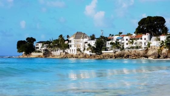 Ocean view of a row of luxury homes in Barbados surrounded by palm trees, blue skies, and stunning crystal waters