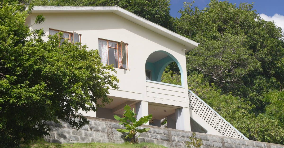 A white house situated on a hill and surrounded by trees. There are windows open on the second floor of the house.