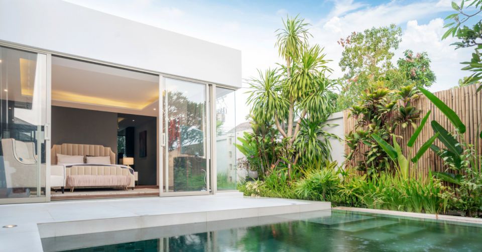 The courtyard of a luxurious tropical villa with a pool and a view of the primary bedroom through sliding glass doors.