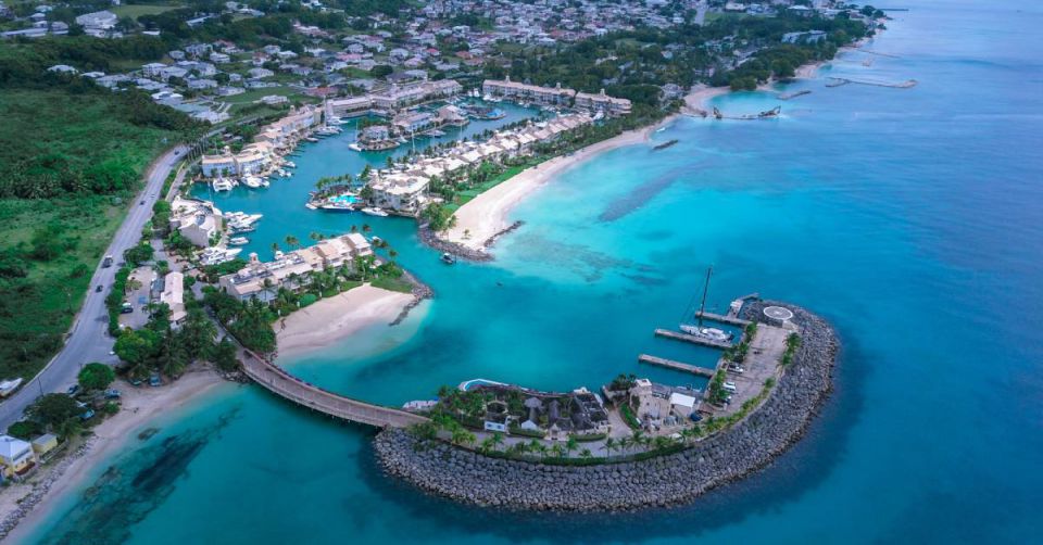 A panoramic view of the Barbados coastline. There are multiple houses and trees visible near white sand.